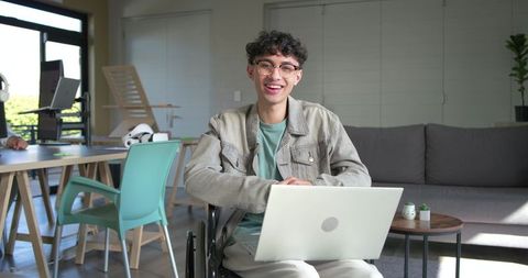 Young professional in wheelchair smiling while working on laptop in modern home office