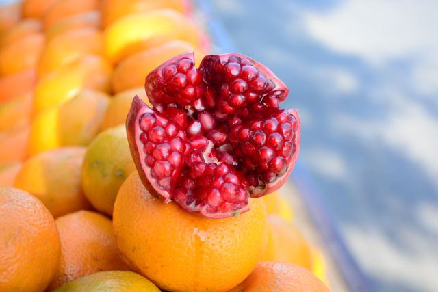 Pomegranate placed on top of oranges at outdoor market, highlighting the contrast between the red pomegranate seeds and orange peel. Perfect for use in health and nutrition articles, farmers market promotions, or fresh produce advertisements.