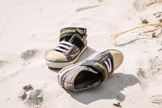 Abandoned child's sneakers on sandy beach evoke memories of summer fun and play near the sea, making it perfect for themes about vacations, childhood, and outdoor activities.
