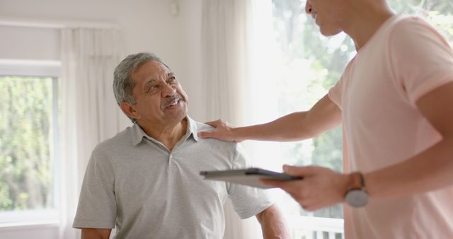 Shows an elderly man engaging in a conversation with a caregiver in a home setting. The scene conveys a sense of comfort, support, and strong relationships, making it suitable for use in articles, advertisements, and websites focusing on elderly care, home support services, senior health, and aging joyfully at home.