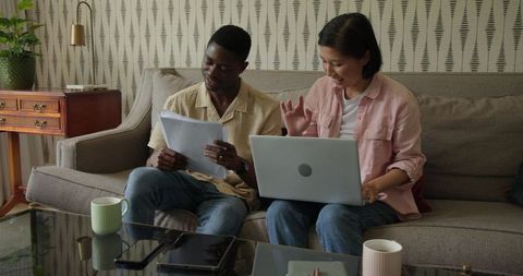 Diverse Team Discussing Ideas with Laptop and Documents on Sofa