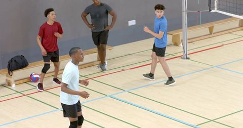 Multiracial male teen volleyball team practicing in indoor gymnasium showing teamwork