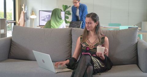 Female professional working on laptop in modern lounge with colleagues collaborating