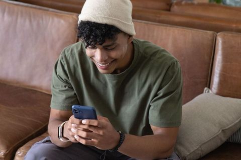 African american man smiling while texting on smartphone on leather couch