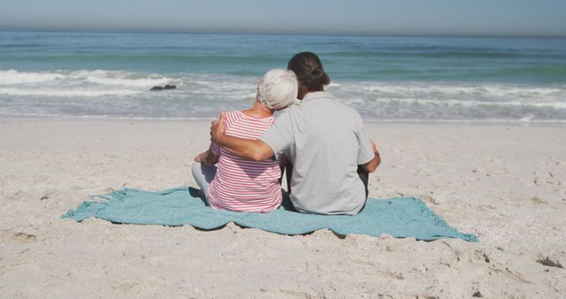 Elderly couple sitting comfortably on beach, looking at ocean horizon. Ideal for themes of retirement, relaxation, leisure time, and quality time in older age. Can be used for travel brochures, retirement community promotions, health and wellness materials, and social media posts celebrating love and companionship in later years.