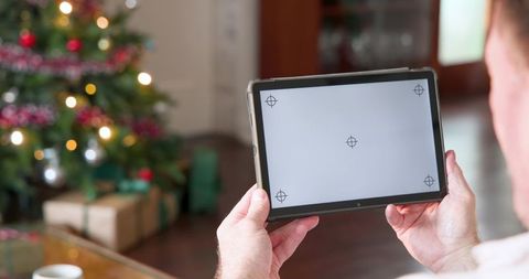 Man holding tablet next to christmas tree at home