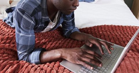 Man Relaxing on Bed Using Laptop in Cozy Bedroom Setting