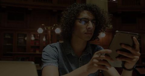 Focused student using tablet at library study table with laptop