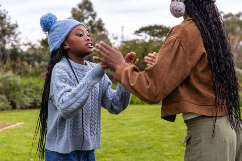 African american mother and daughter playing clapping game wearing knit beanies on lawn
