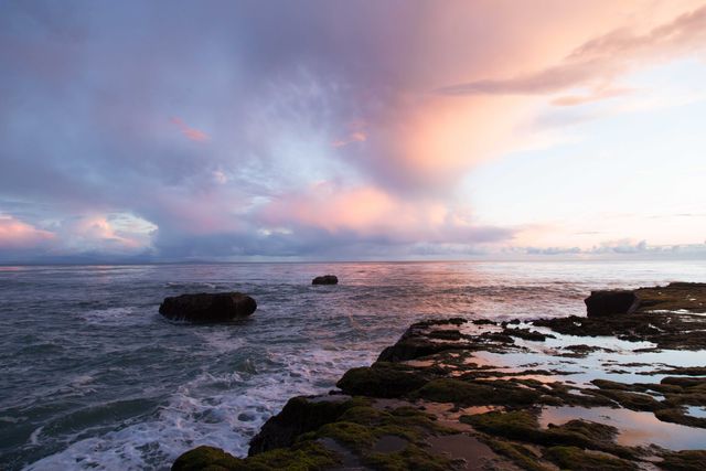 Captures a serene sunset over the ocean with a dramatic sky and rocky shoreline. Ideal for use in nature photography, travel blogs, environmental awareness campaigns, posters, and social media posts celebrating natural beauty.
