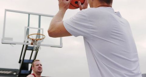 Adult male shooting basketball on urban outdoor court with defender and hoop in background
