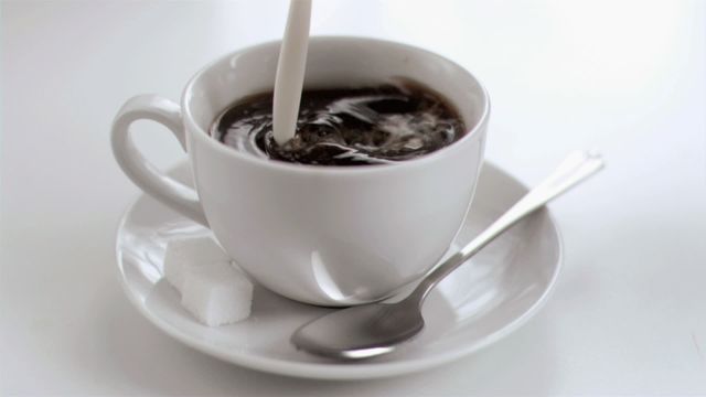 Milk dripping in slow motion into a coffee cup against a white background showcases a delicate and inviting imagery. Suitable for coffee-related advertisements, morning breakfast decor, cafe promotional material, or barista training visuals.