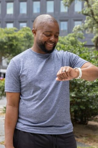 Smiling man checking smartwatch in urban plaza with modern office building and greenery