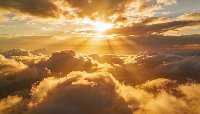 Golden sunbeams glowing over layered cumulus clouds at high altitude panoramic sky