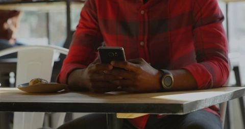 Casual man using smartphone with smartwatch in cafe