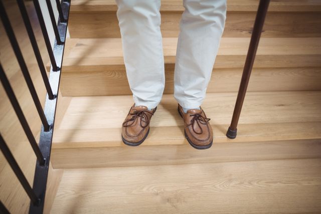 Senior man carefully climbing downstairs with the aid of a walking stick at home. This image can be used to illustrate topics related to elderly care, mobility support, home safety, and independent living for seniors.