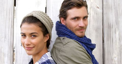 Happy diverse couple smiling back to back by rustic wooden wall