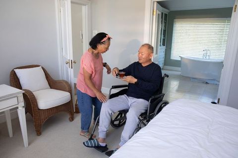 Senior asian couple sharing tea at home while man in wheelchair receiving care and support