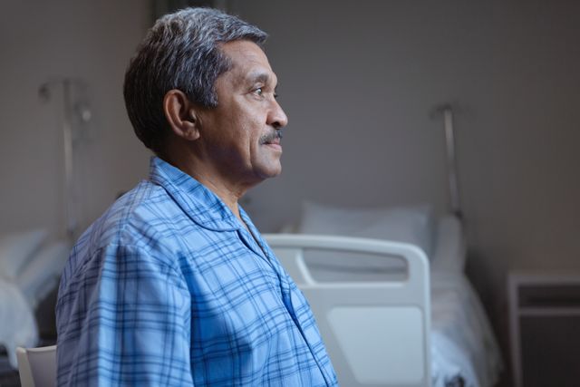 Side view of mature male patient sitting on medical bed and looking away in medical ward at hospital