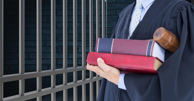Judge in robe holds legal books and gavel near jail cell, representing concepts of justice, law enforcement, and the judicial system. Ideal for use in articles, legal publications, or awareness on judicial processes and legal procedures.