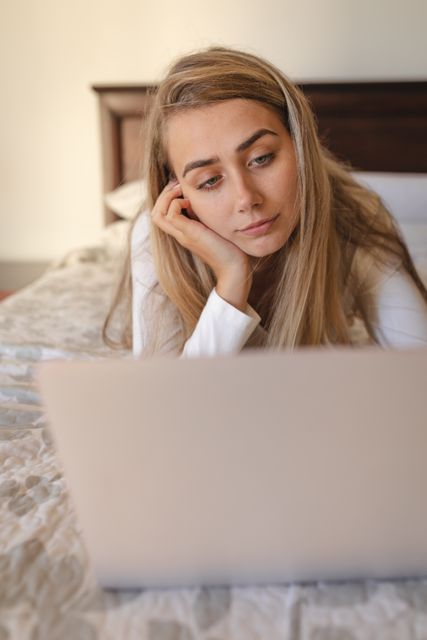Caucasian woman spending lying on bed using laptop computer. Social distancing and self isolation in quarantine lockdown during coronavirus Covid 19 pandemic.