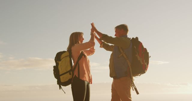 Happy senior caucasian couple hiking with backpacks high fiving at sundown, copy space. Celebration, relationship, retirement, vacations, wellbeing and active senior lifestyle, unaltered.