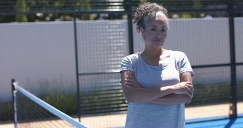 Confident woman standing on paddle tennis court crossing arms in casual sportswear