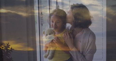 Mother Embracing Daughter by Window With Teddy Bear