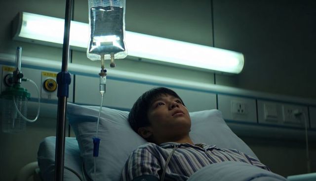 Asian teen patient lying in hospital bed gazing at iv bag under fluorescent light