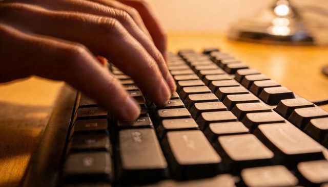 Warm closeup showing hands typing on keyboard pressing textured keys at wooden desk