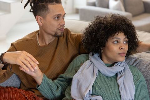 Diverse couple holding hands on sofa in cozy modern living room, intimate moment