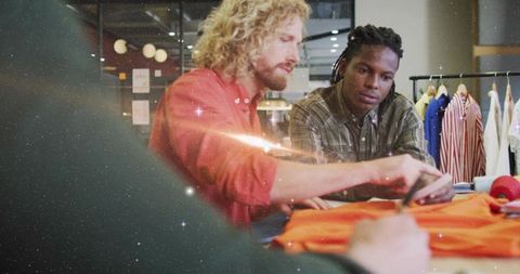 Designers collaborating on bright orange garment, trimming, pattern cutting in studio