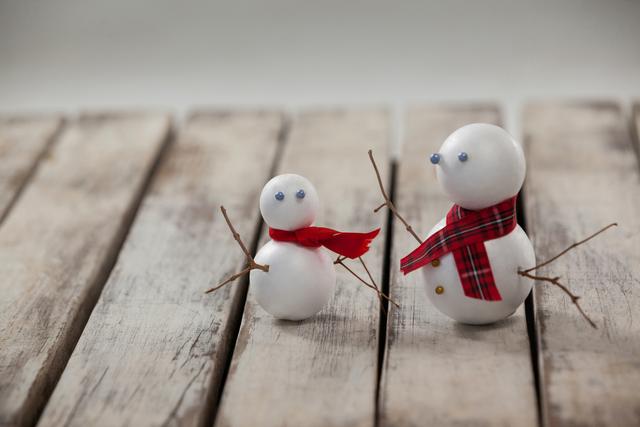 Two snowmen with red scarves standing on a wooden plank. Perfect for holiday cards, winter-themed decorations, or festive social media posts. The image evokes a sense of family and togetherness during the winter season.