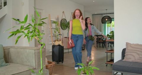Diverse friends entering bright modern living room with rolling suitcase and excited smiles