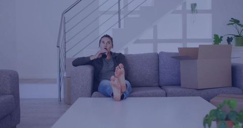 Young woman relaxing on modern sofa amid moving boxes at home