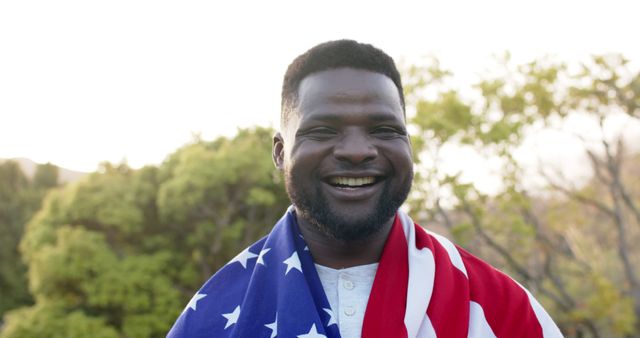 Image shows a man wrapped in an American flag while smiling outdoors, conveying patriotism and pride. Suitable for themes related to American holidays like the 4th of July, Veteran's Day, or Memorial Day. Ideal for use in campaigns emphasizing national pride, inclusivity, and unity. Can be utilized by blogs, social media, and advertisements centered around American culture and public celebrations.