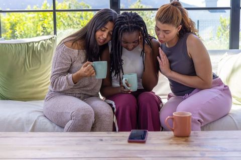Comforting circle of diverse women holding mugs offering support and empathy on sofa