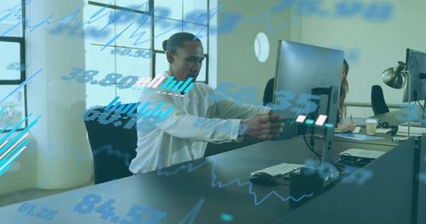 Man adjusting monitor at office desk with financial charts overlay and team workspace