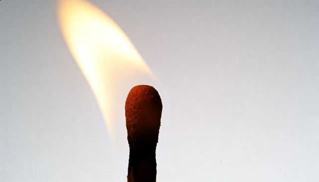Burning Match Close-Up with Charred Tip and Leaning Yellow Flame on White Backdrop