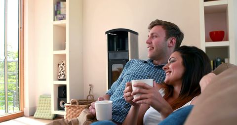 Young Couple Relaxing on Couch With Coffee in Cozy Home Setting