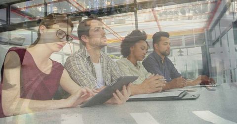 Collaborating team reviewing notes with tablet and laptop in modern glass conference room