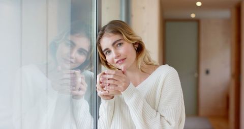 Woman relaxing at home holding ceramic mug near window