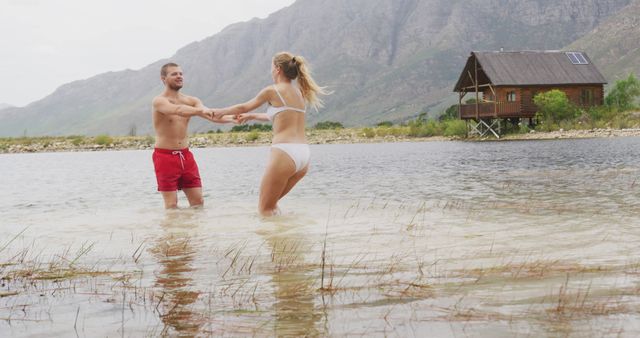 Caucasian couple dancing in lake water and holding hands with copy space. Nature, travel, tranquility, lifestyle concept, unaltered.