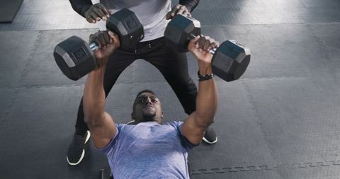 African american male bench pressing with trainer in gym