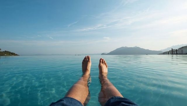Relaxing feet in infinity pool overlooking sea and mountains at luxury coastal villa