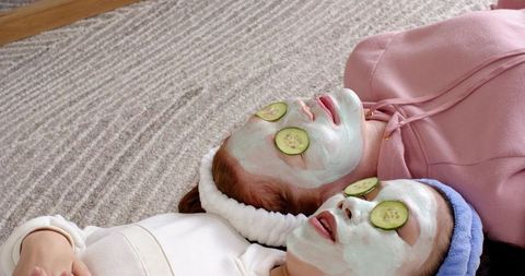 Friends enjoying at-home spa day wearing mint face masks and cucumber slices