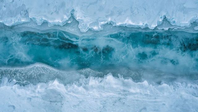 Turquoise melt channel slicing arctic sea ice, aerial polynya with slushy foam bands