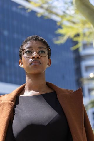 African-american businesswoman standing confidently by glass office building with glasses