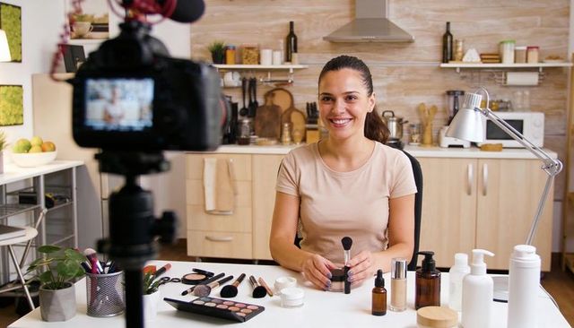 Filming beauty tutorial in home kitchen, smiling female creator demonstrating makeup tips