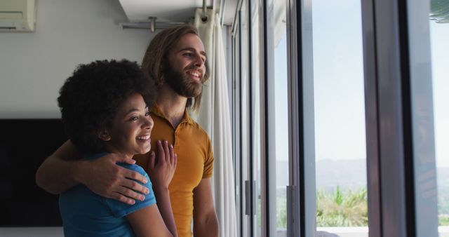 Biracial couple looking out of the window at home. staying at home in self isolation in quarantine lockdown